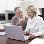 Happy middle aged couple calculating home finances on laptop at kitchen table