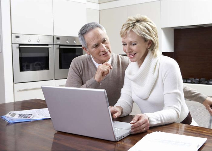 Happy middle aged couple calculating home finances on laptop at kitchen table