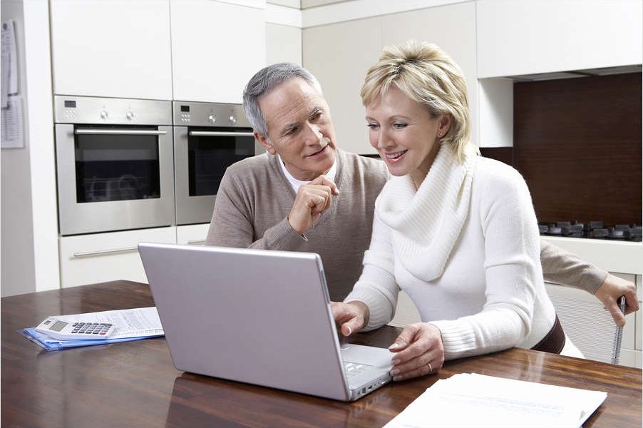 Happy middle aged couple calculating home finances on laptop at kitchen table